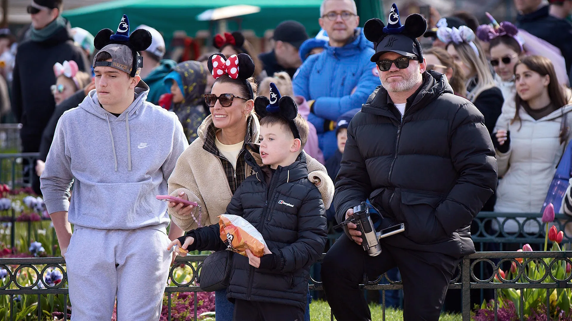Wayne Rooney and Coleen Rooney stand with family members wearing Mickey Mouse ear headbands at Disneyland Paris in The Real Rooneys.