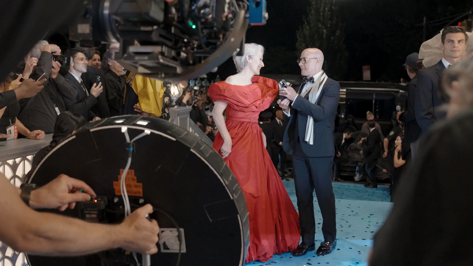 Miranda Priestly (Meryl Streep) wears a red dress while attending a fashion event with Nigel (Stanely Tucci).
