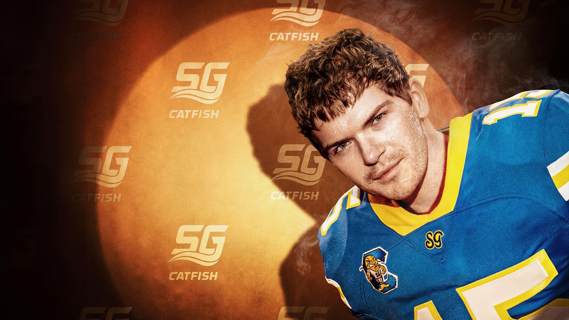 Gerry Dougan (Colton Ryan) olha para frente com um leve sorriso irônico, vestindo uma camisa de futebol americano azul e amarela do "SG CATFISH", em frente a um fundo laranja vibrante.
