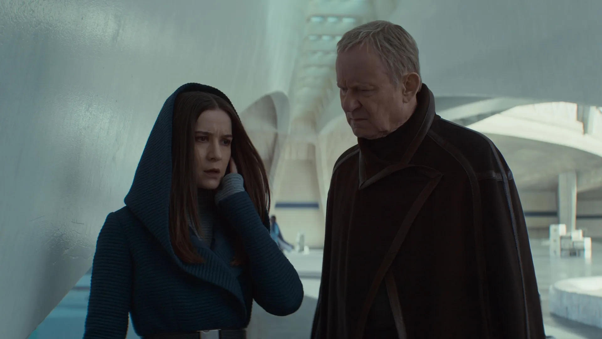 A hooded Kleya (Elizabeth Dulau) and Luthen (Stellan Skarsgård) wai outside the senate building on Coruscant.