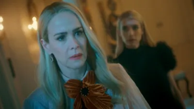 Cordelia Goode stands in the foreground while Madison Montgomery stands behind her inside a candlelit room in American Horror Story: 13.