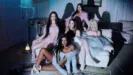 Five members of the global girl group KATSEYE—Megan, Lara, Yoonchae, Daniela, and Sophia—pose dramatically in a dimly lit, retro-styled bedroom with blue and white overhead lighting.