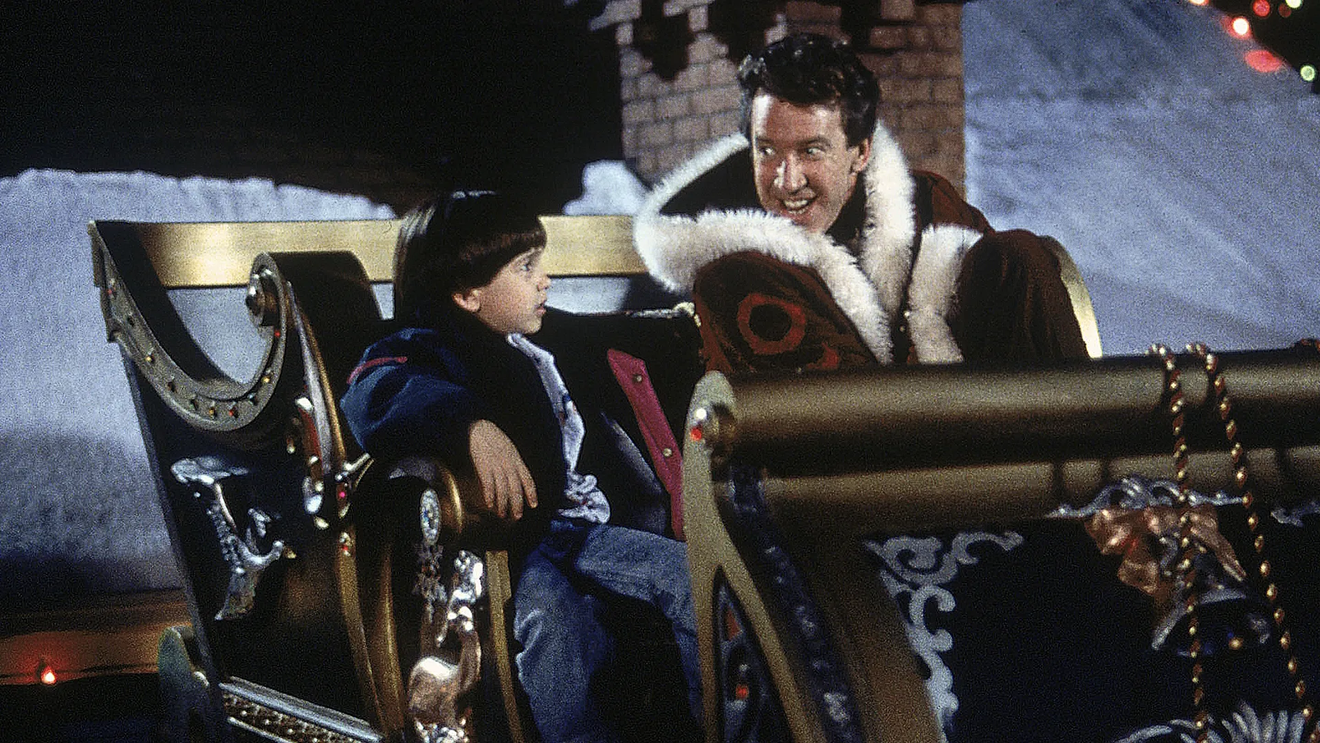 Scott Calvin (Tim Allen) sits in Santa's sleigh with his son Charlie on the roof of a house.