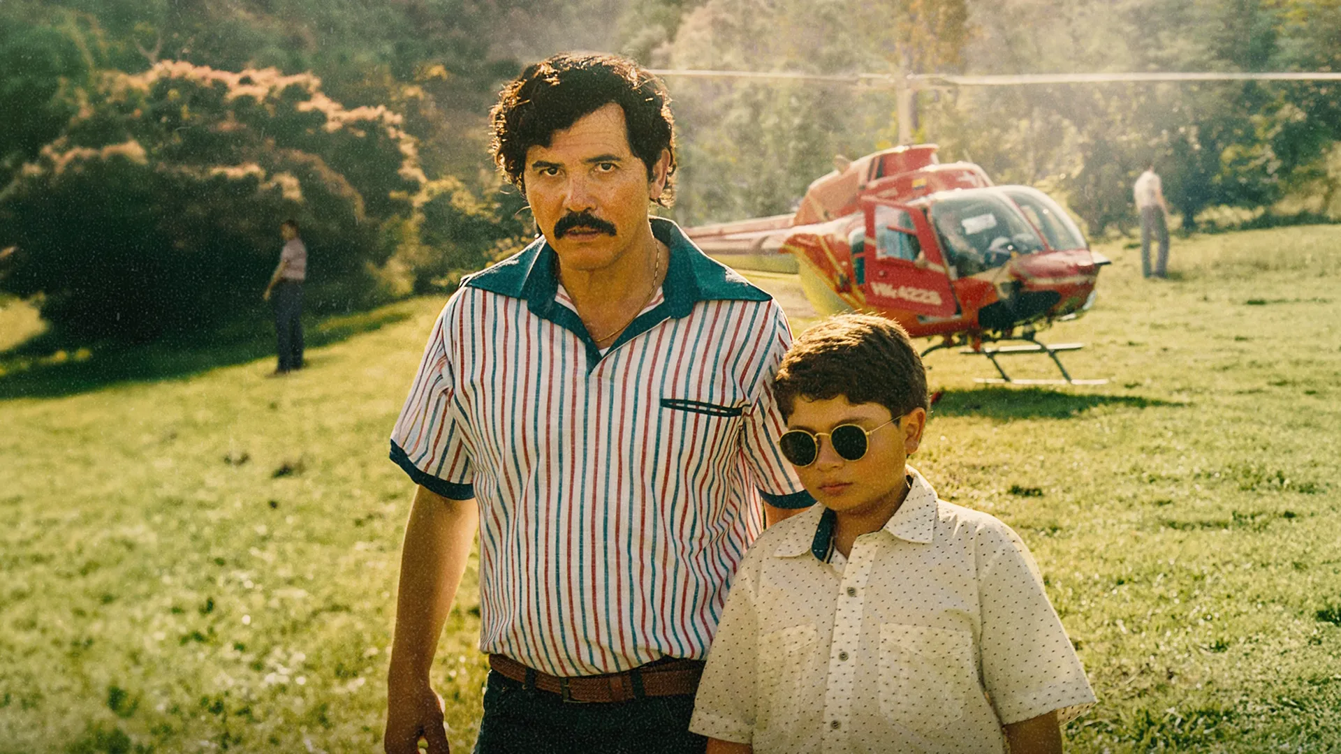 This image features John Leguizamo portraying the infamous drug lord Pablo Escobar alongside his son in a still from the drama series Dear Killer Nannies (originally titled Dear Killer Nannies: Criado por sicarios)