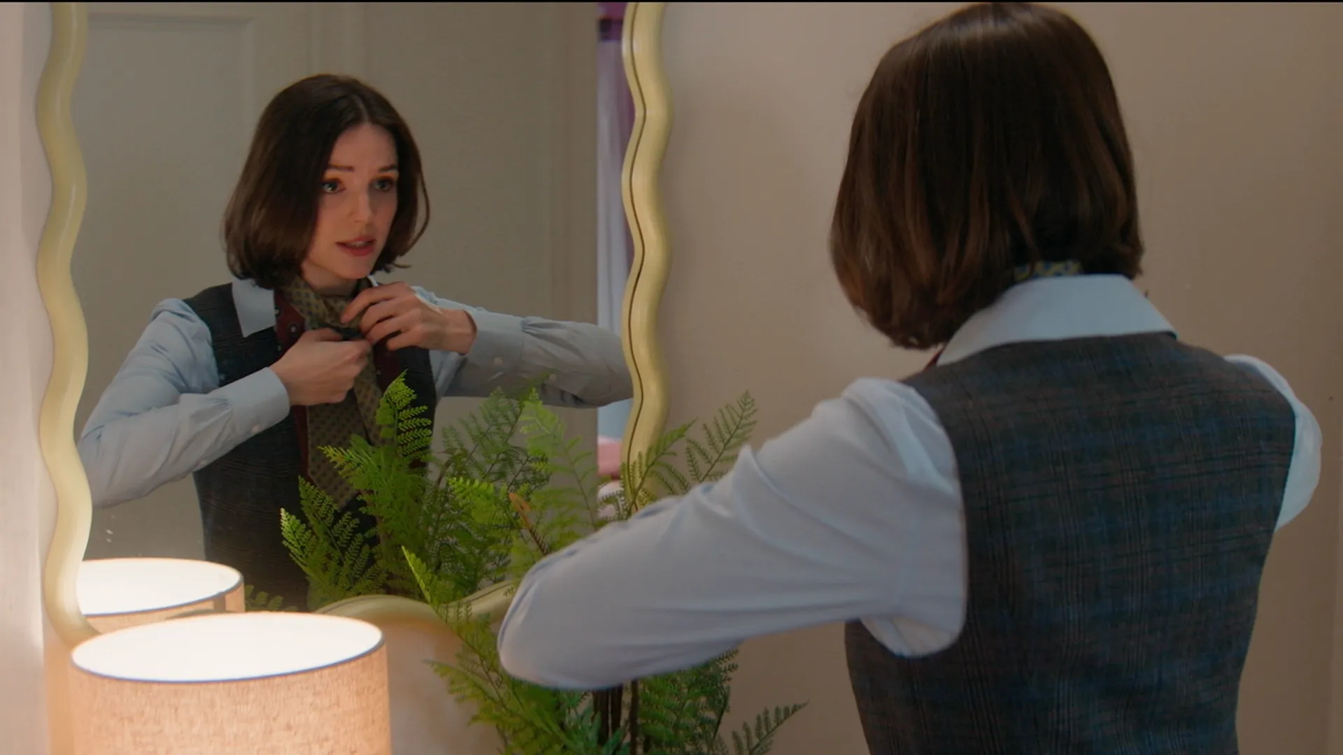 AJ Pascarelli (Ella Hunt) ajeita a gravata, se olhando no espelho.