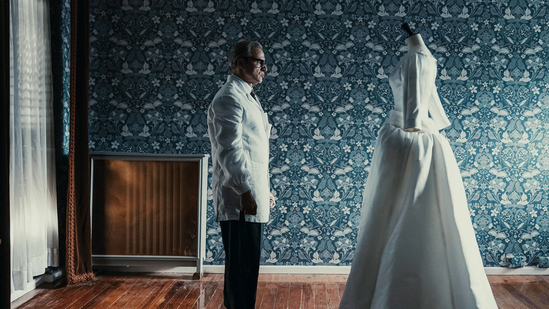 Cristóbal Balenciaga (Alberto San Juan) looks over a long white dress on a mannequin.