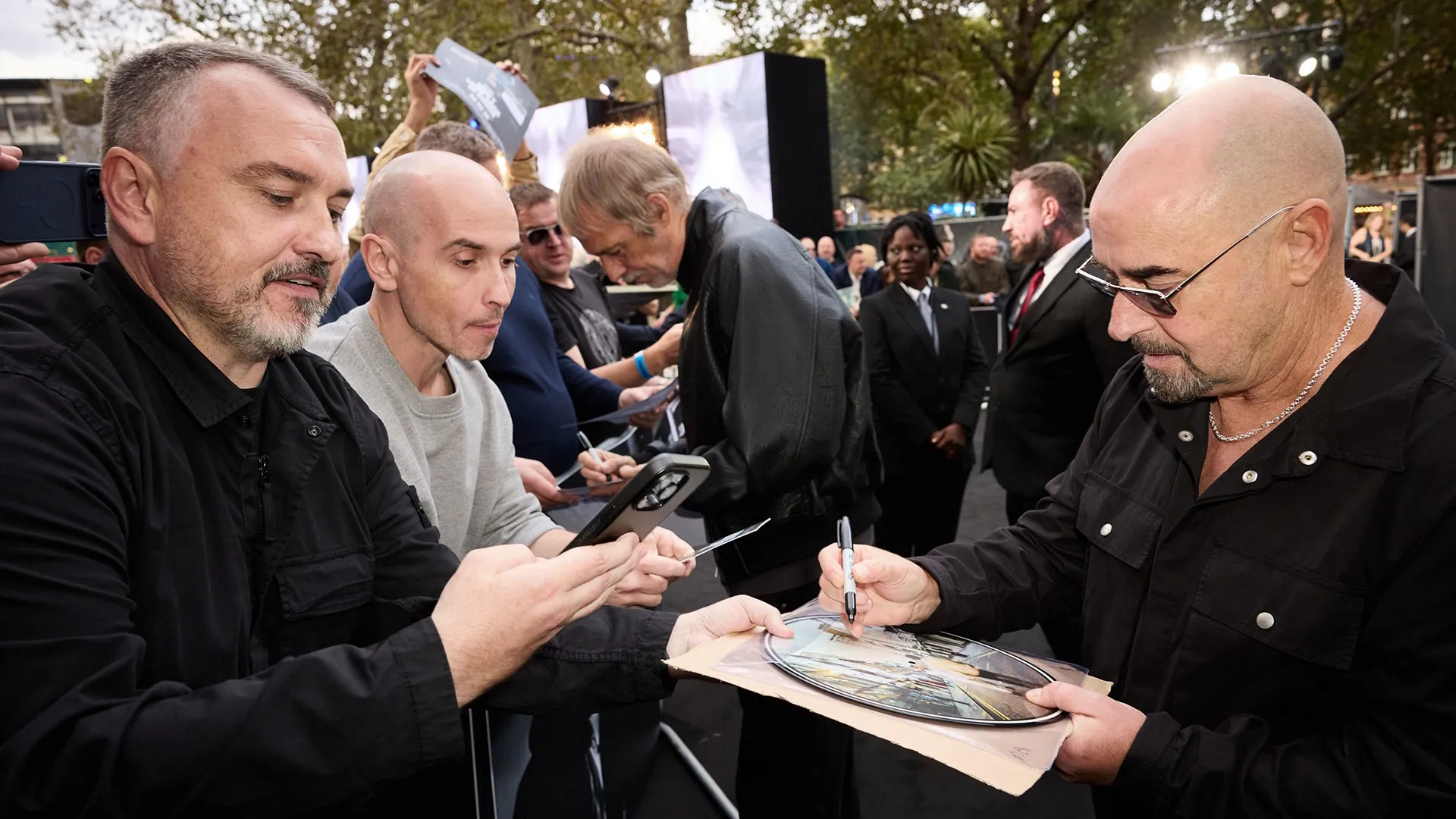 Paul 'Bonehead' Arthurs signs memorabilia for fans at the London premiere of Oasis: Don’t Look Back in Anger.