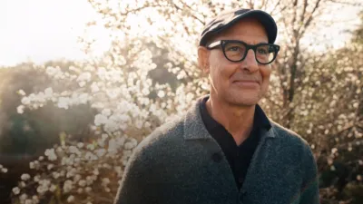 A closeup of Stanley Tucci with a sunlit blossoming tree background