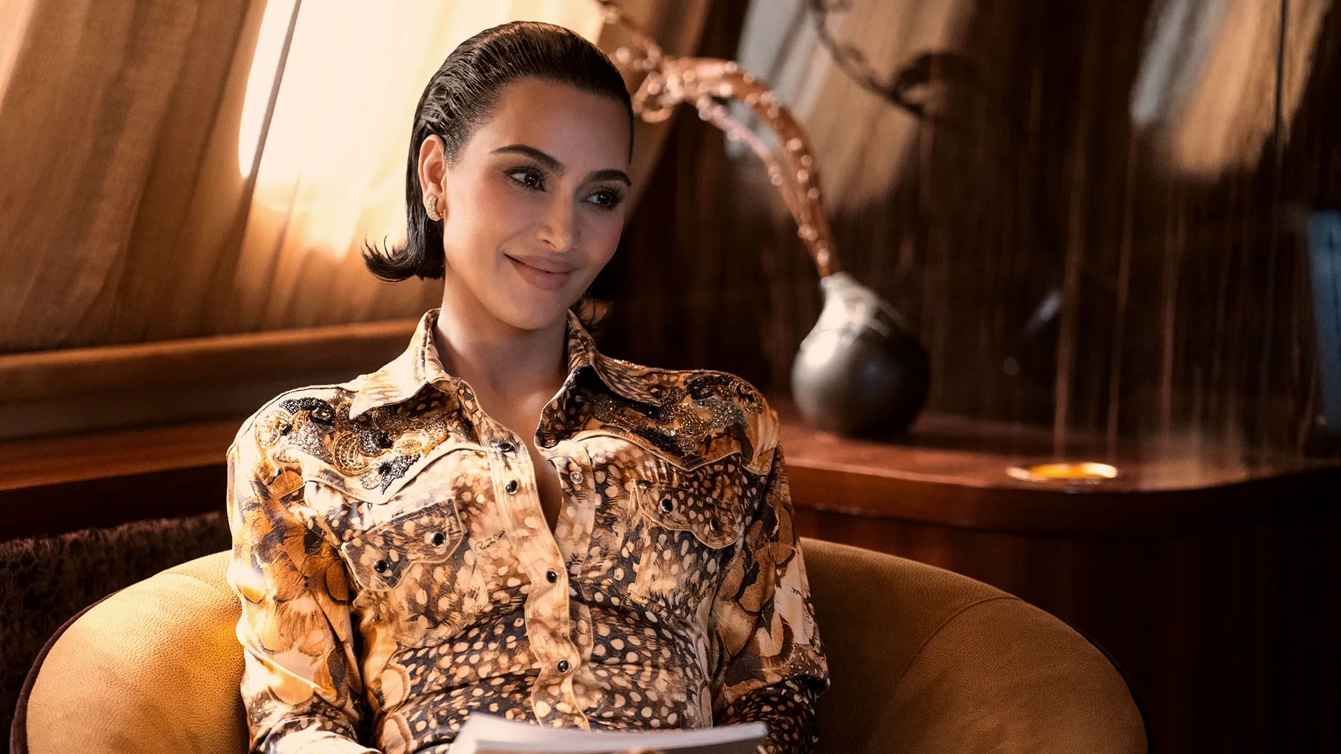 Kim Kardashian as Allura Grant in a short, slicked-back bob and patterned blouse