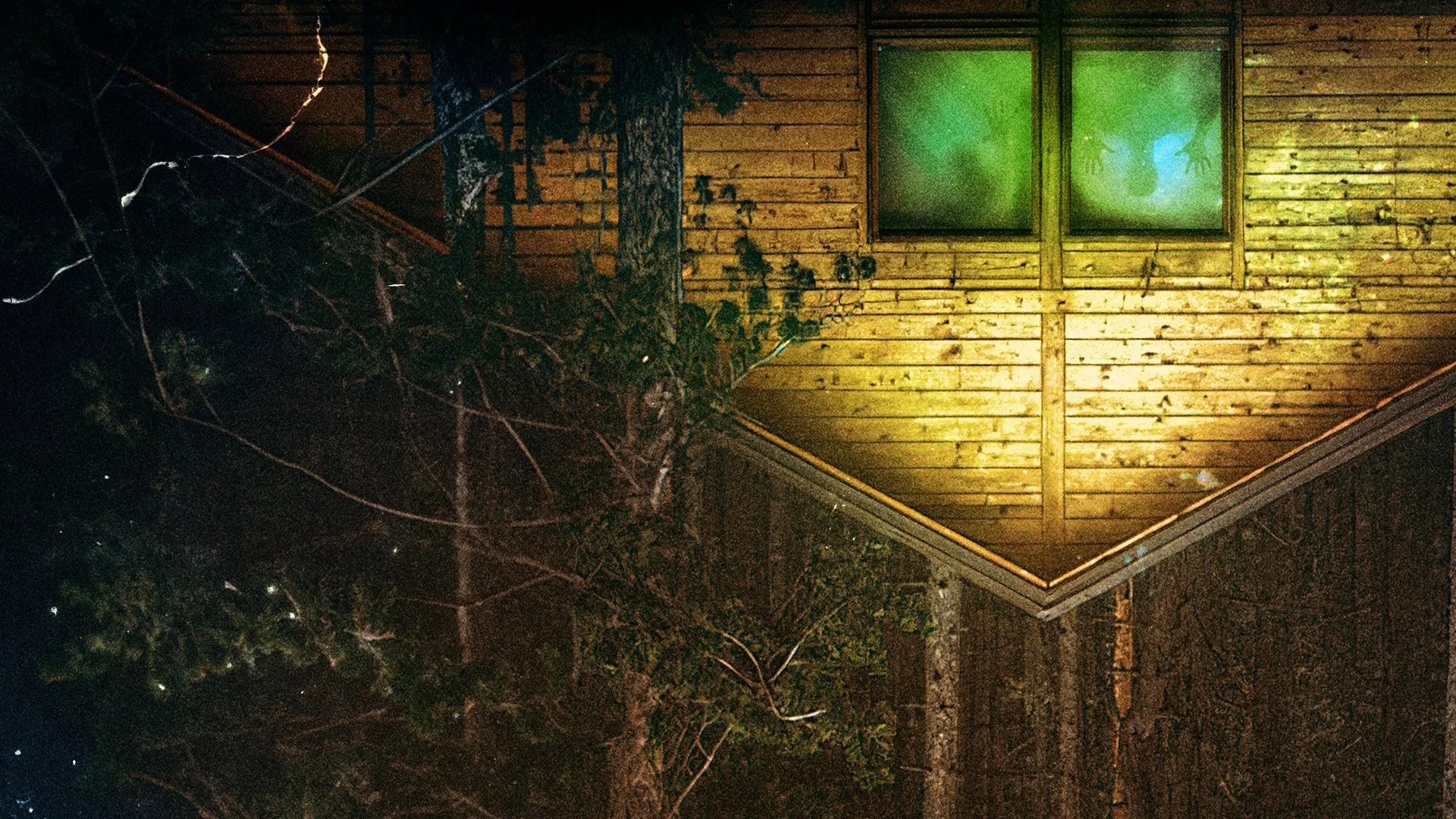 An upside-down perspective of a rustic wooden cabin at night, featuring a window glowing with an eerie green light where shadowy hands press flat against the glass pane.