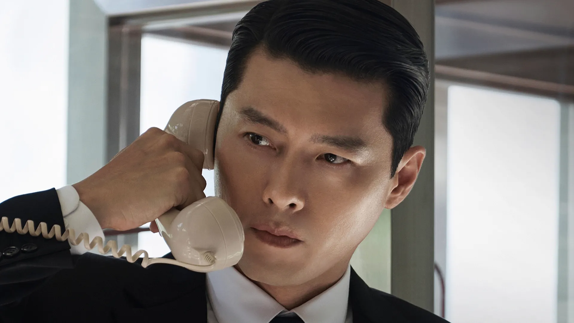 Hyun Bin as Baek Gi-tae wearing a professional suit and holding an old phone to his ear from Made in Korea.