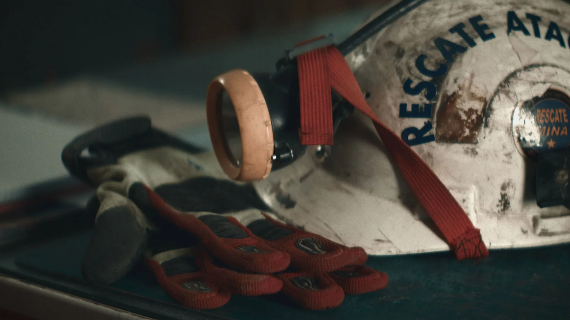 A mining helmet with a headlamp and a pair of work gloves rest on a metal surface.