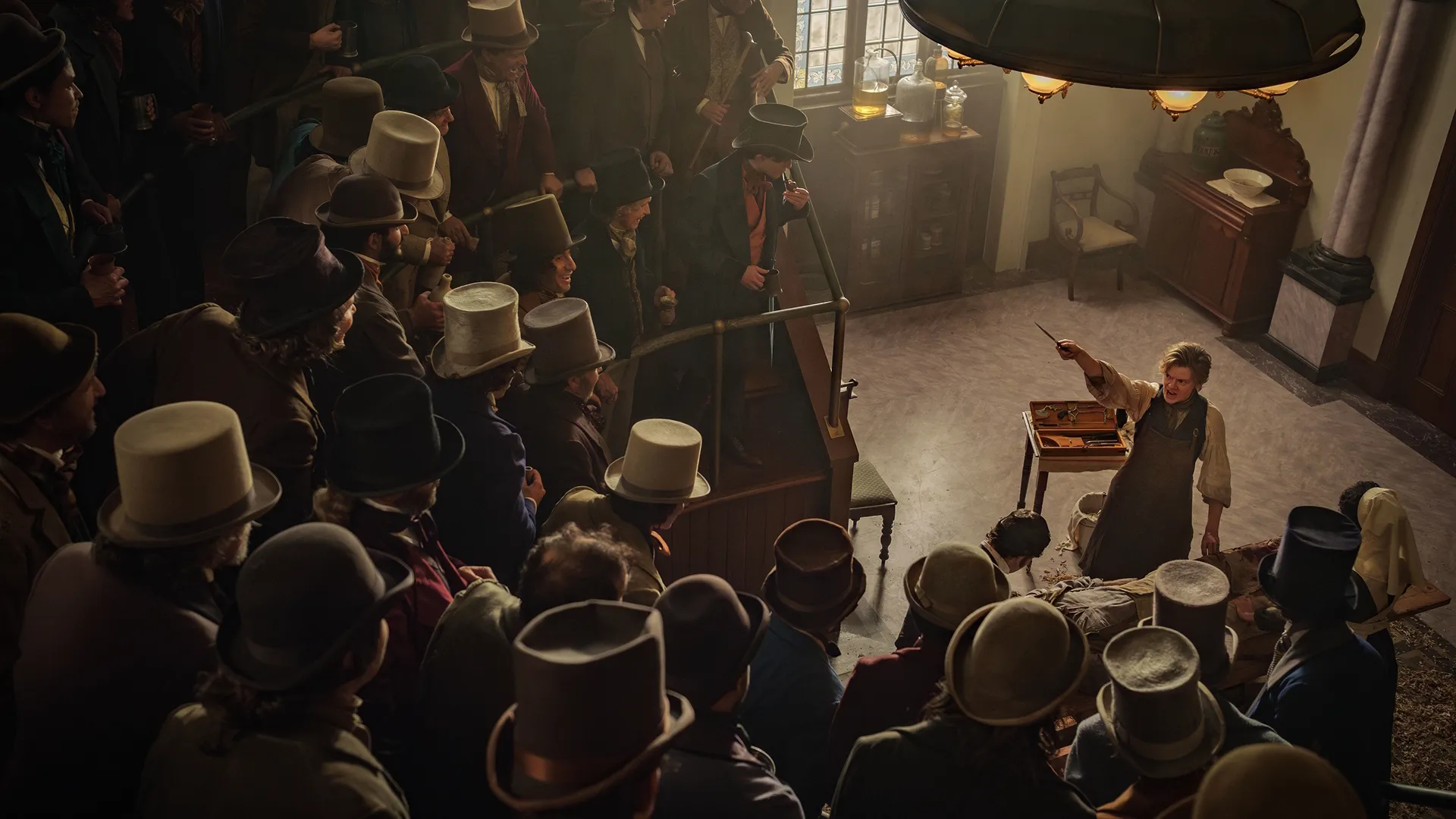 Artful Dodger (Thomas Brodie-Sangster) stands at the centre of a Victorian surgeon's hall, pointing a scalpel at the crowd