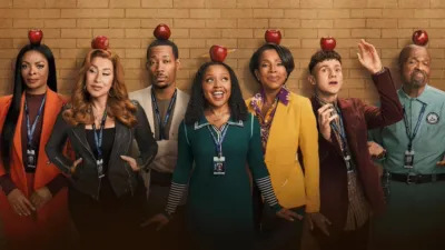 Abbott Elementary main cast promotional photo for Season 3 featuring Janelle James, Lisa Ann Walter, Tyler James Williams, Quinta Brunson, Sheryl Lee Ralph, Chris Perfetti, and William Stanford Davis balancing red apples on their heads in front of a brick wall.