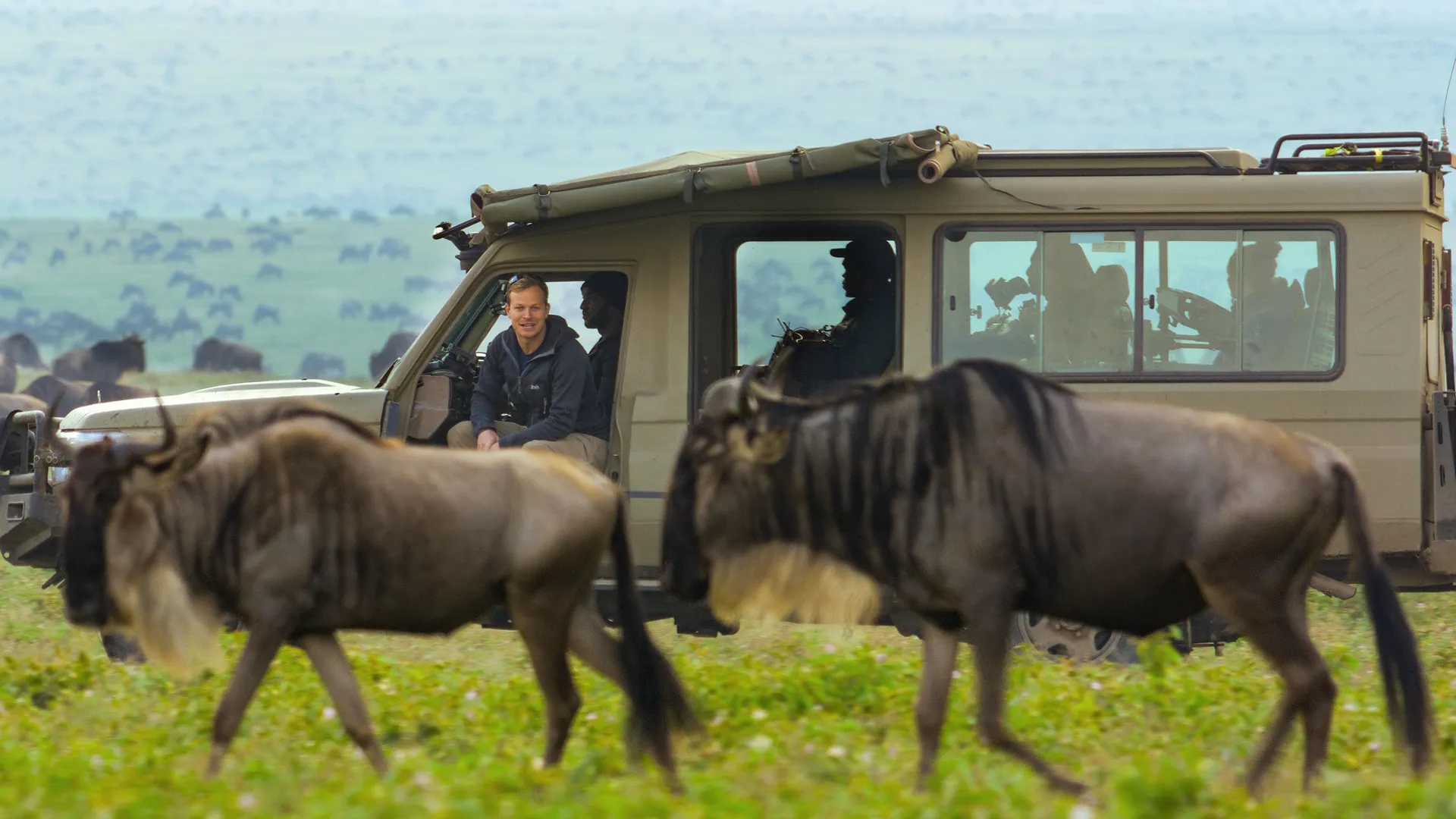 Bertie Gregory sits in his safari Jeep with his crew watching the wildebeest walk past.  (credit: National Geographic/Tom Walker)