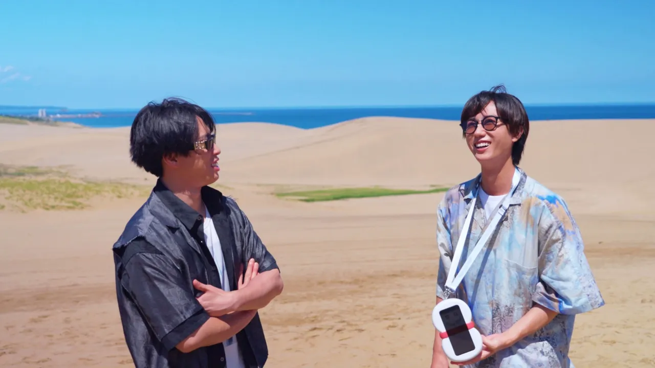 Snow Manのメンバー2人が鳥取の砂丘で海を背に会話している様子。