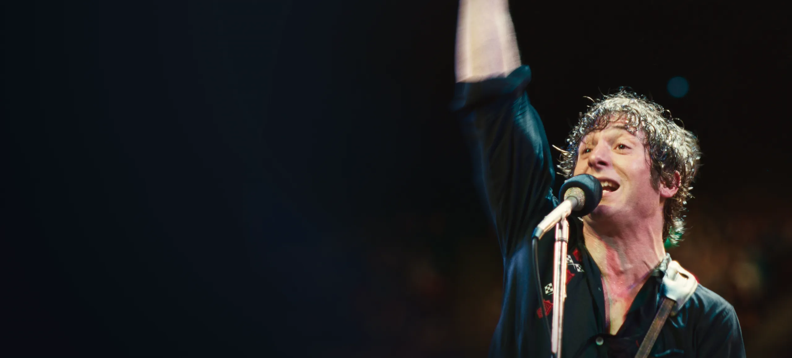 Bruce Springsteen (Jeremy Allen White) plays a guitar in front of a microphone.