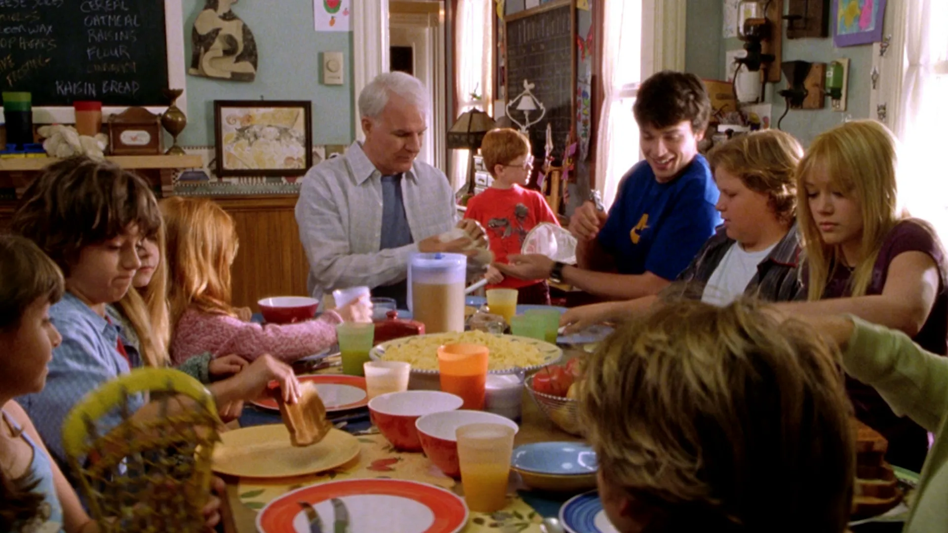 Una ajetreada escena del desayuno familiar de Más barato por docena muestra a Tom Baker (Steve Martin) sentado en la mesa llena de comida y tazas de colores, rodeado por varios de sus doce hijos, entre ellos Charlie (Tom Welling) y Lorraine (Hilary Duff)