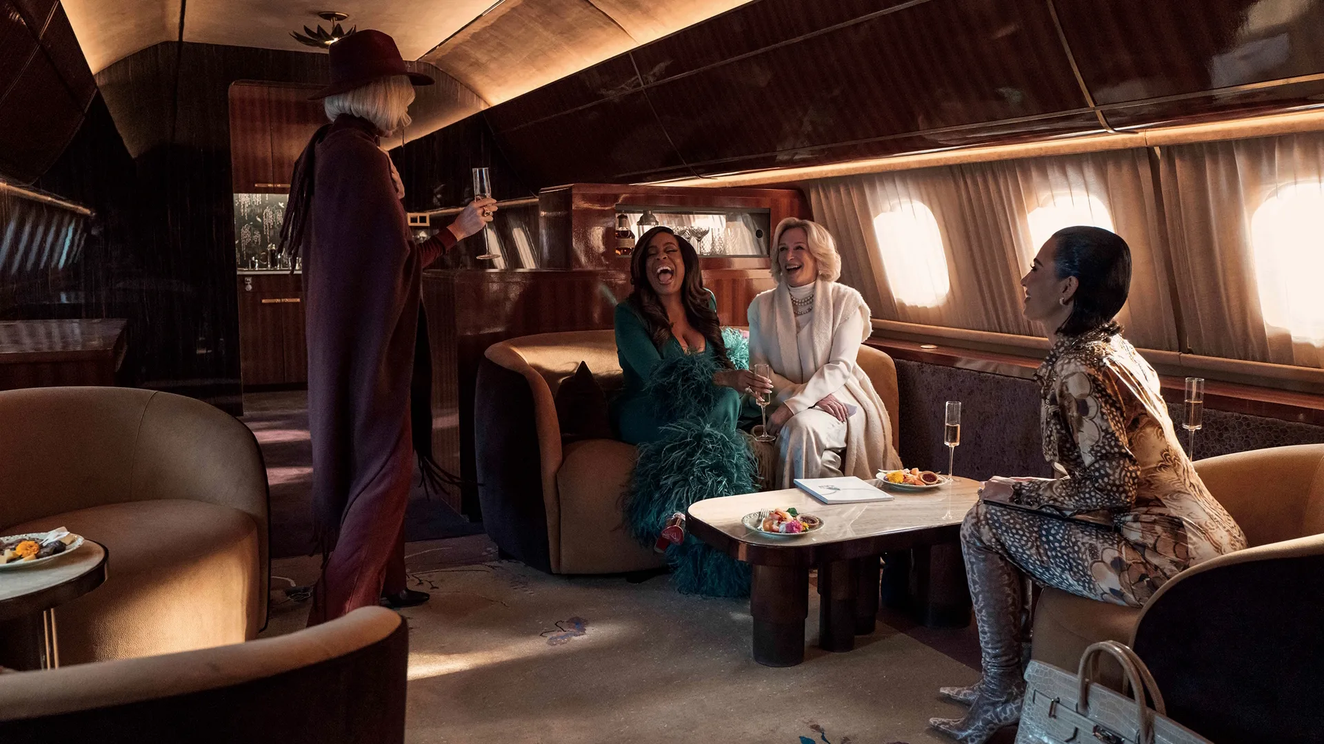 Four characters from All's Fair on a private plane drinking champagne together.
