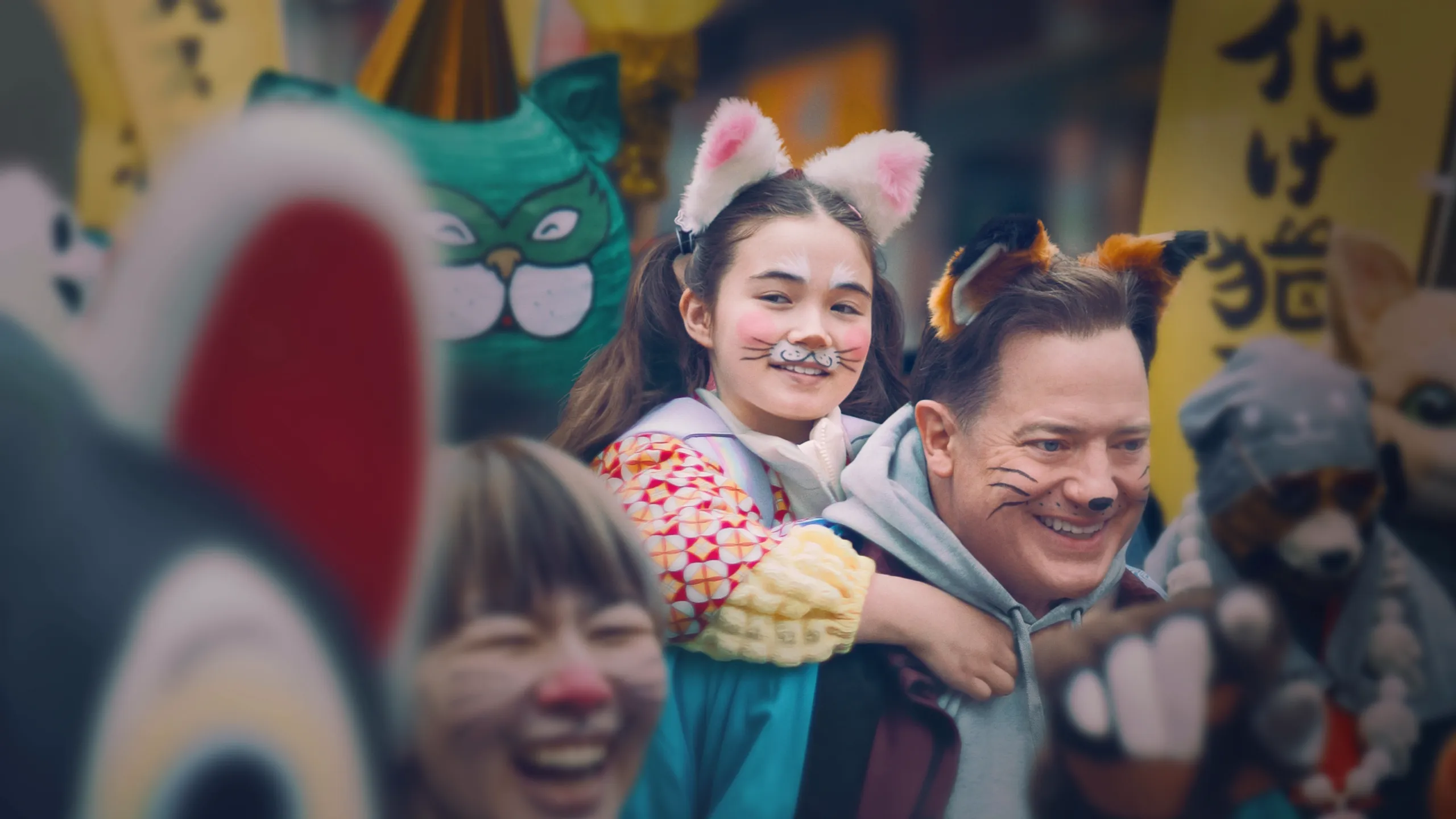 Phillip (Brendan Fraser) is carrying Mia (Shannon Mahina Gorman) on his back. Both are smiling and have their faces painted