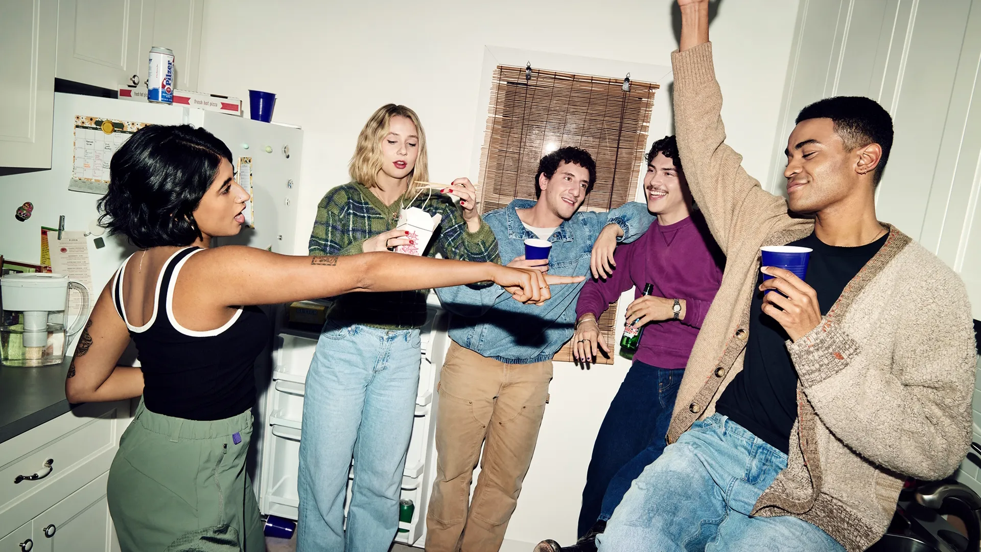 A lively group of five young adults gathering and socializing in a brightly lit kitchen during a house party.