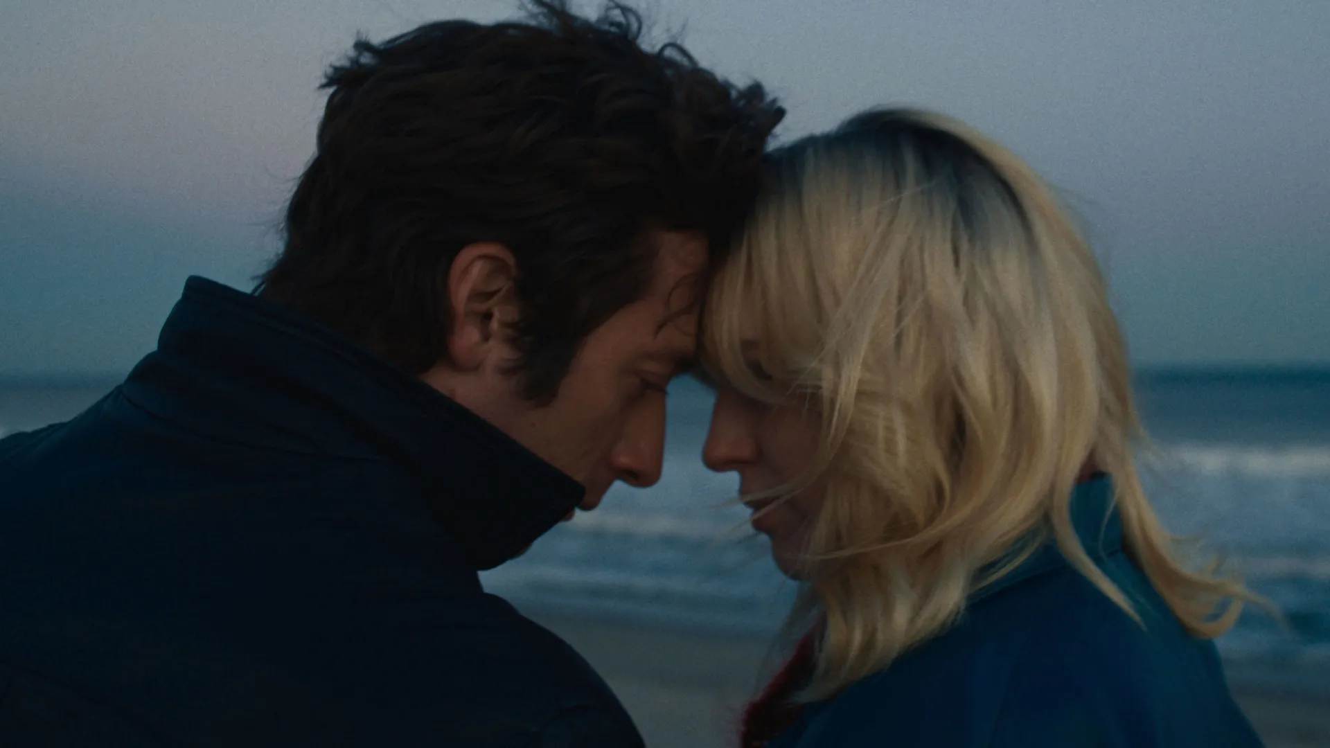 Bruce Springsteen (Jeremy Allen White) and Faye Romano (Odessa Young) touch their foreheads together by the sea at dusk.