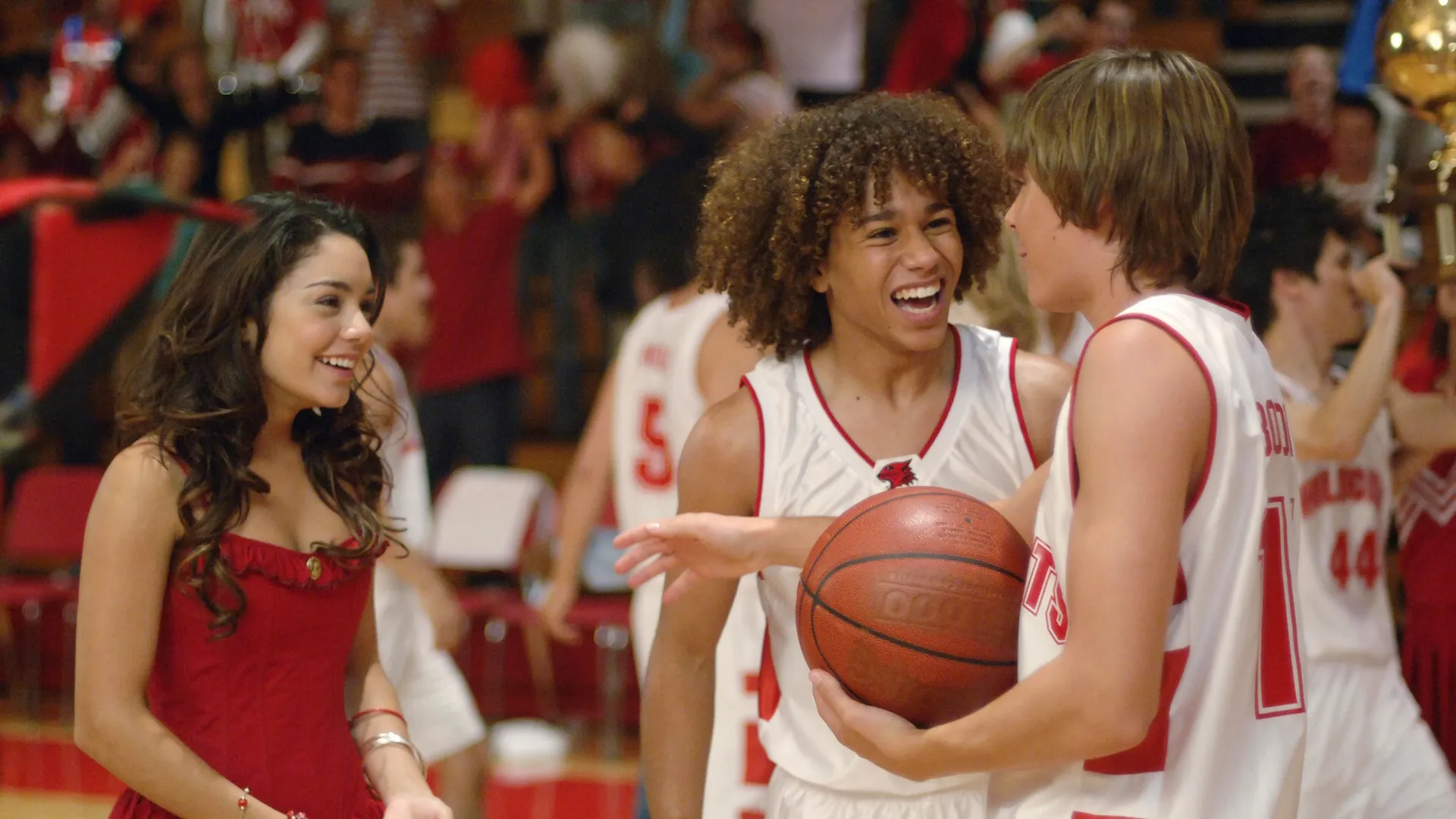 Troy (Zac Efron), holding a basketball, talks to Gabriella (Vanessa Hudgens) and Chad (Corbin Bleu) on the school basketball court
