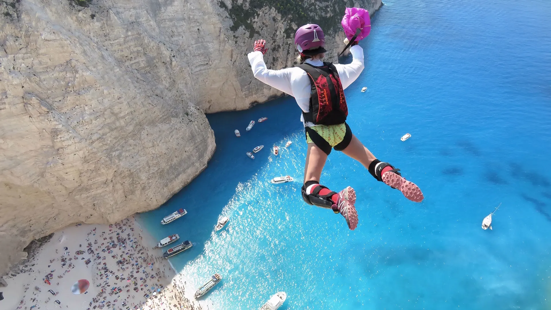 A base jumper opens their parachute mid-jump as people watch in the cove below.