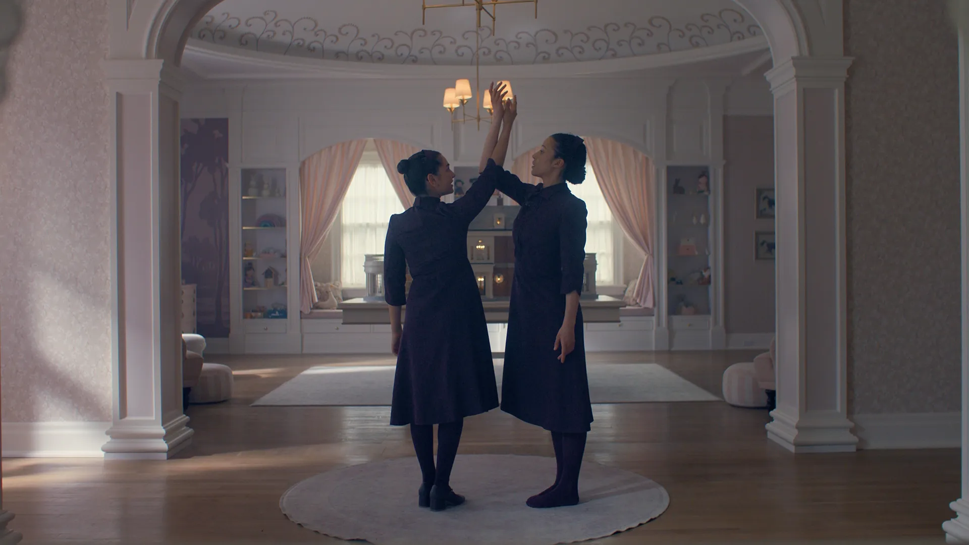 Two characters from the Testaments holding their hands in the air in the centre of a room