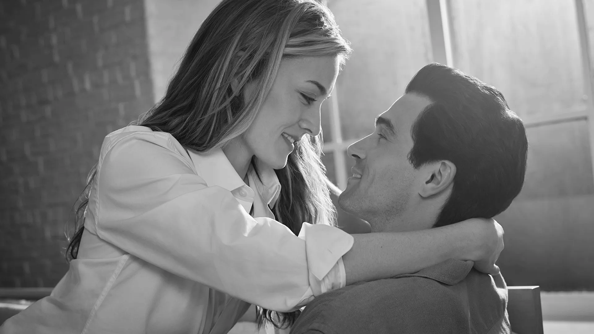 Carolyn Bessette (Sarah Pidgeon) and John F. Kennedy Jr. (Paul Kelly) embrace in a black and white set photo from FX's Love Story.