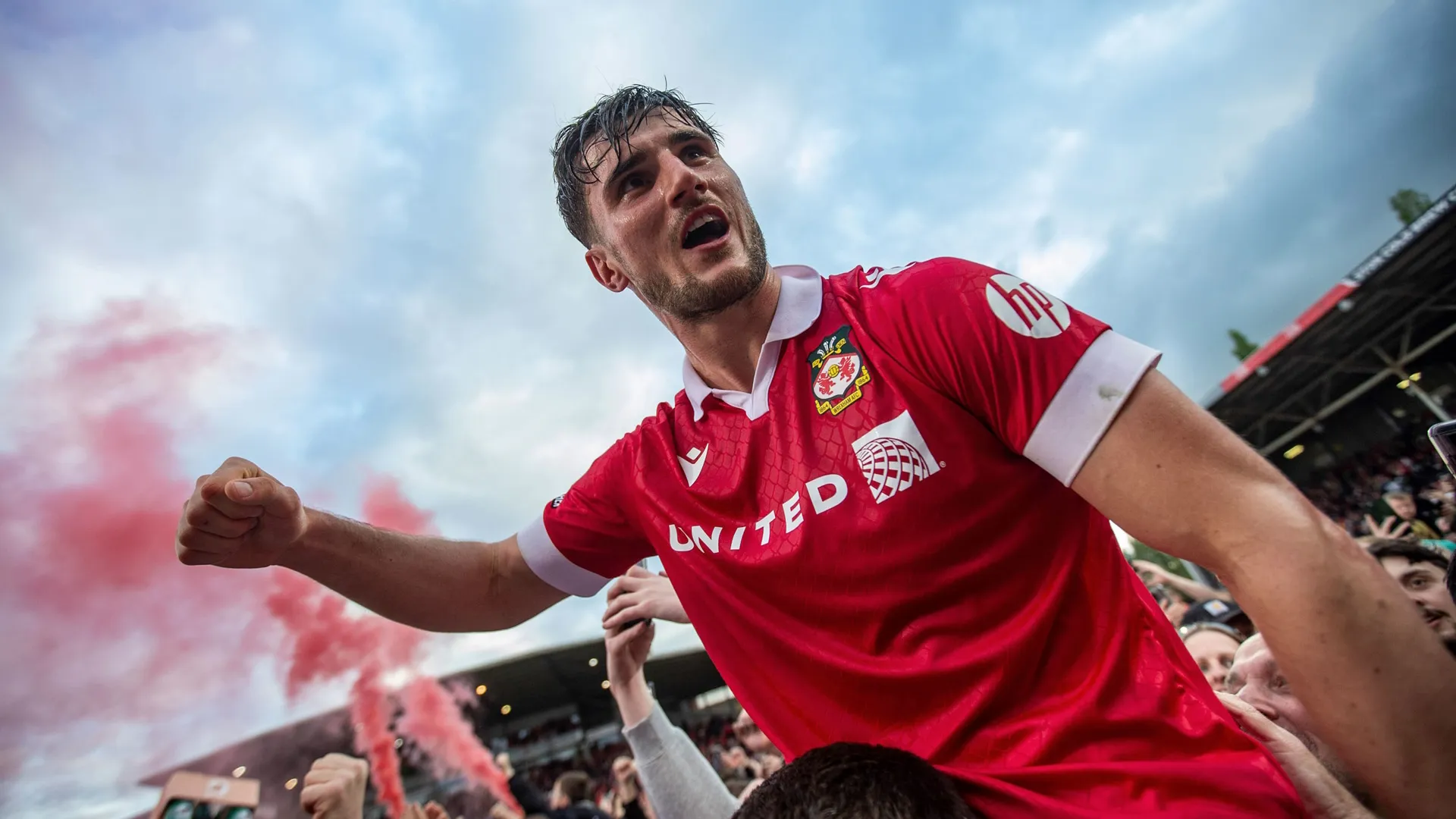 A Wrexham player cheers as red flare goes off in the background.