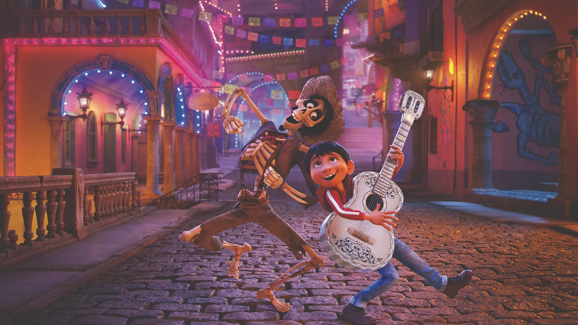 En esta escena callejera animada de Coco, iluminada de forma vibrante, Miguel (Anthony Gonzalez) sonríe mientras sostiene una guitarra acústica blanca junto a Héctor (Gael García Bernal), un esqueleto con ropa andrajosa y sombrero de paja, mientras posan en una calle de adoquines decorada con coloridas pancartas festivas y luces brillantes