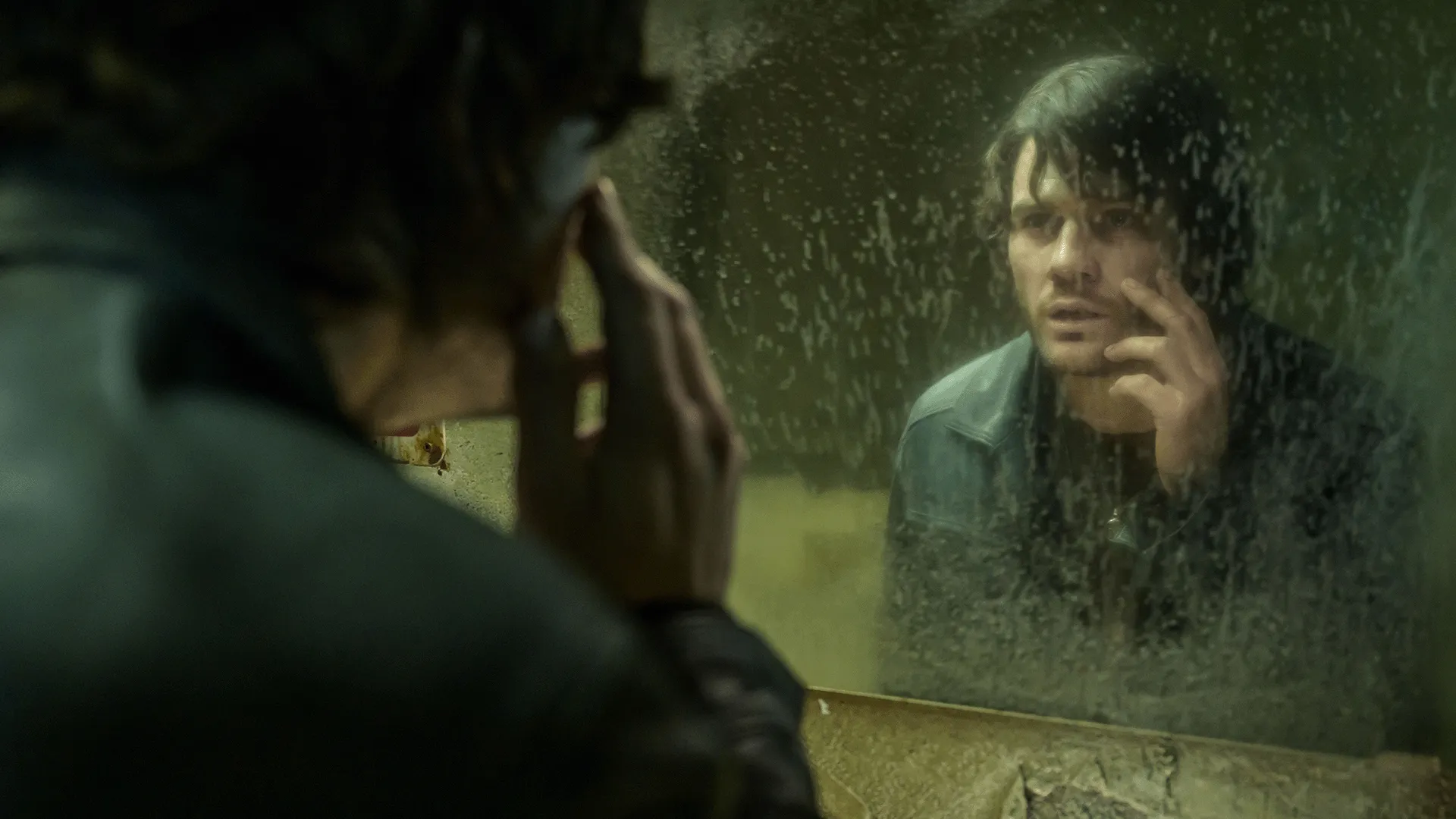 James Sunderland (Jeremy Irvine) looking at his own intense, troubled reflection in a heavily weathered and dirty bathroom mirror.