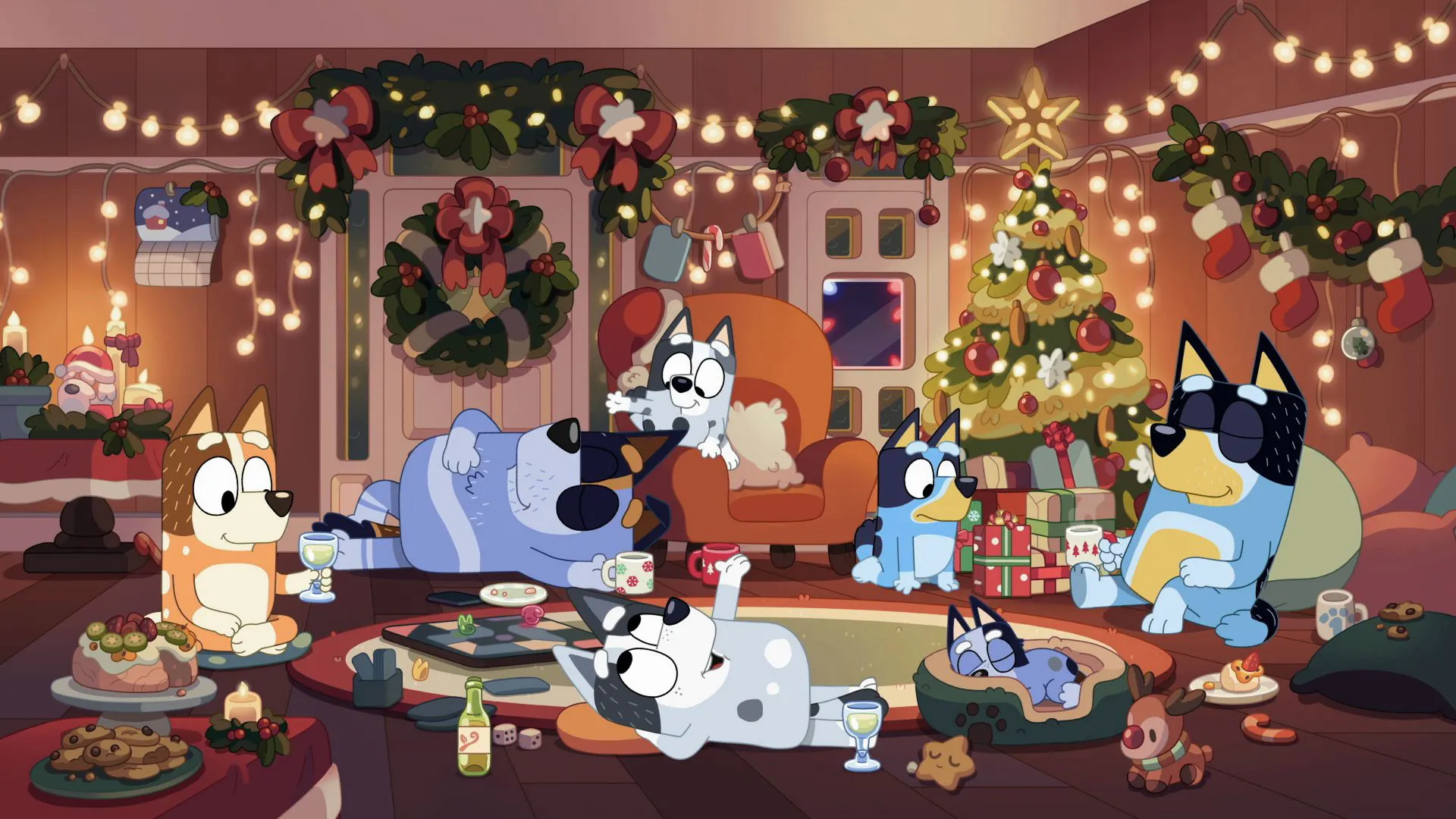 The Heeler family and extended relatives relax on the floor of a festively decorated living room filled with string lights, a Christmas tree, and holiday treats.