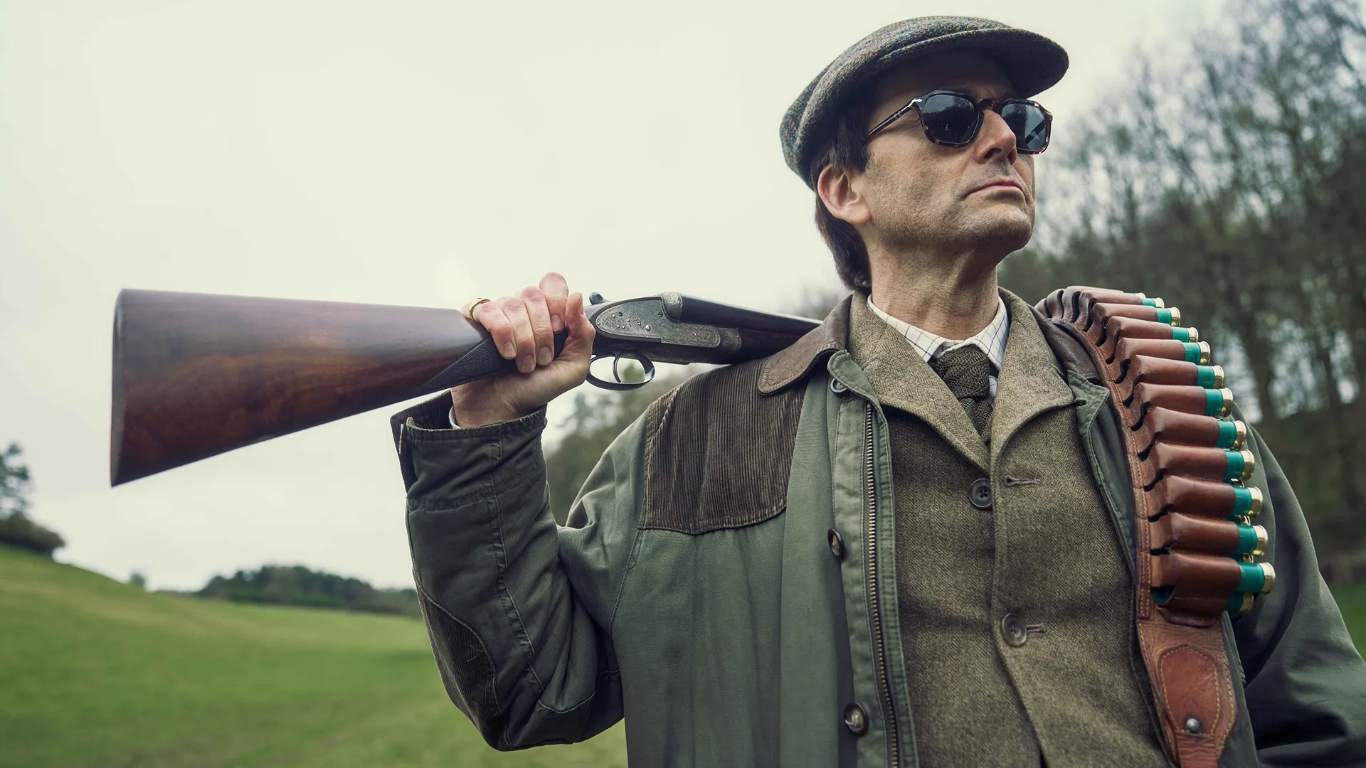 Tony Baddingham (David Tennant) with a hunting rifle slung over his left shoulder. 