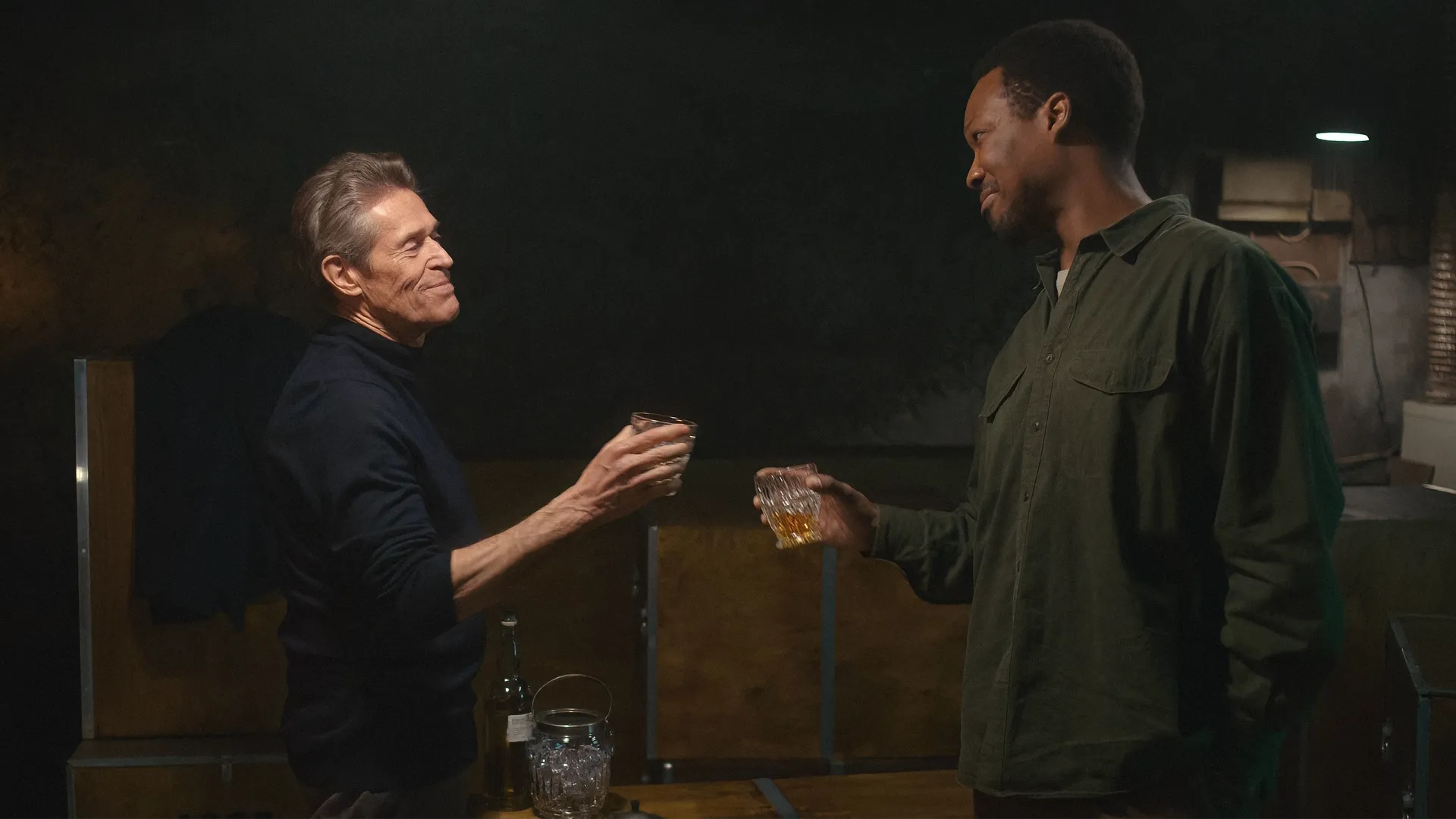 Willem Dafoe and Corey Hawkins sharing a toast in the psychological thriller film The Man in My Basement.