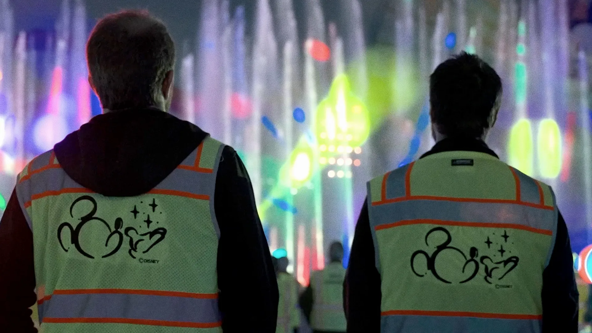 This image shows two workers wearing safety vests on the set of We Call It Imagineering, Disney+