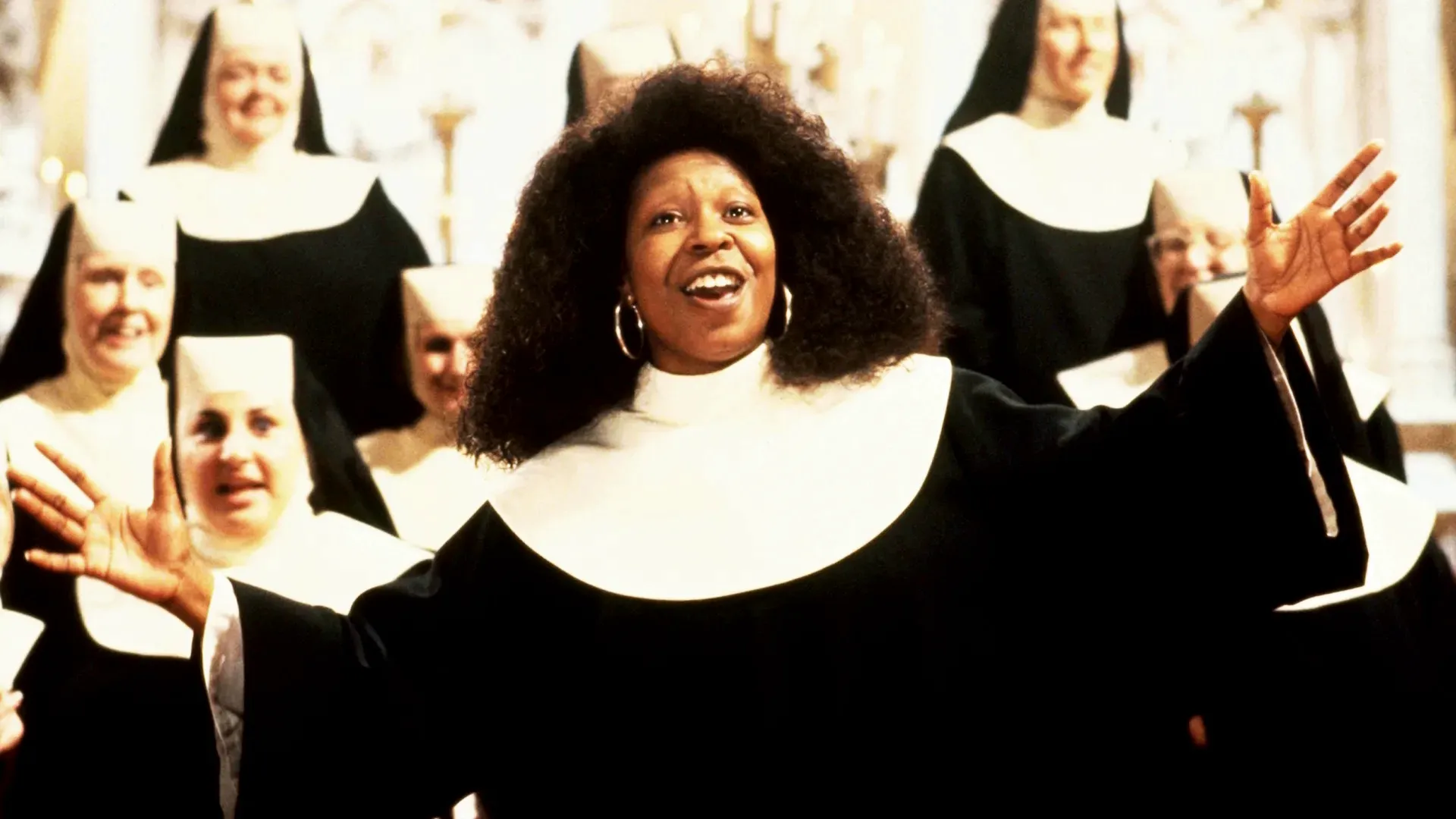 Deloris Van Cartier (Whoopi Goldberg) at the head of a group waving her hands, in the middle of song.