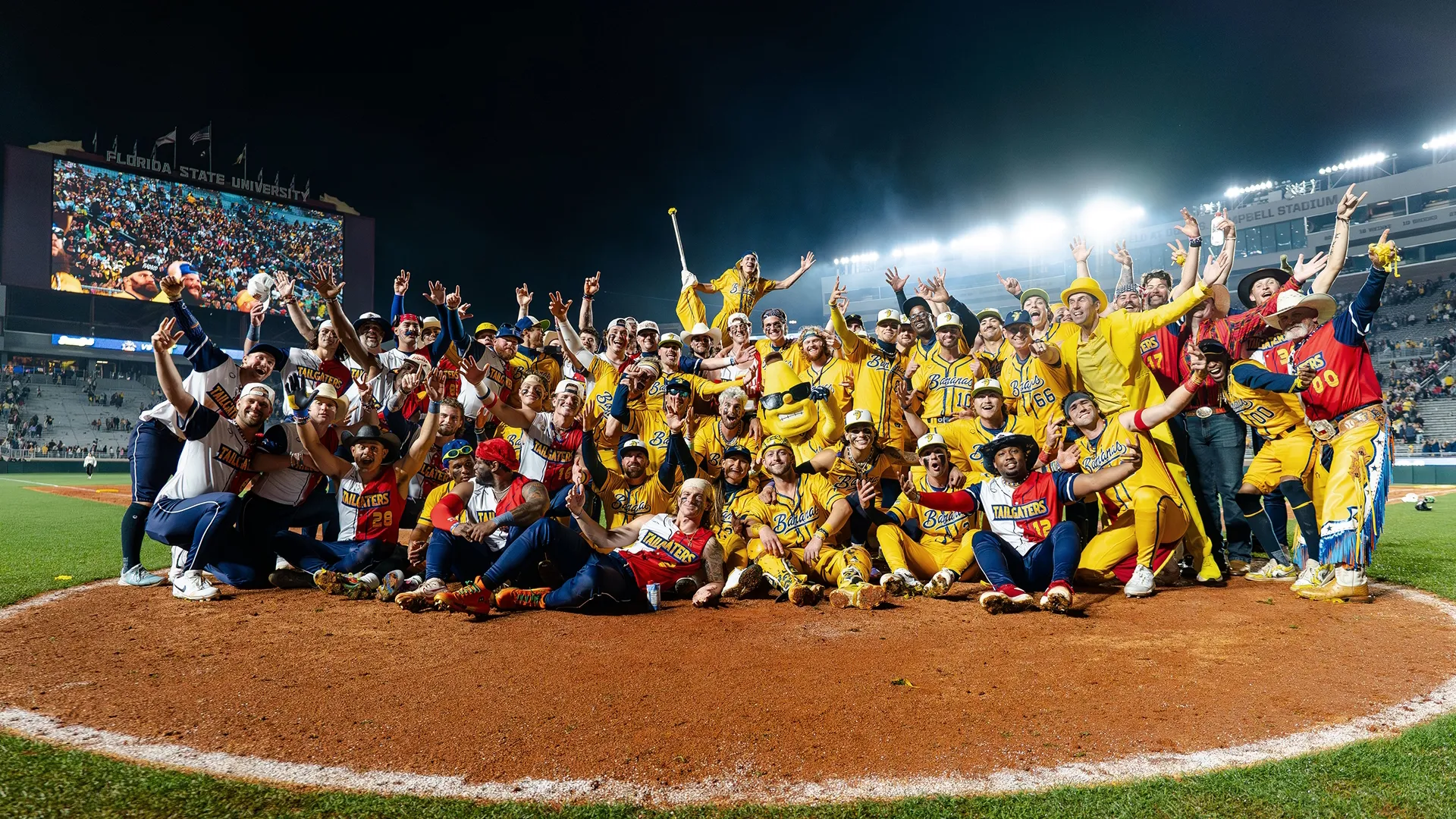 The Savannah Bananas crowd together in the center of the field.