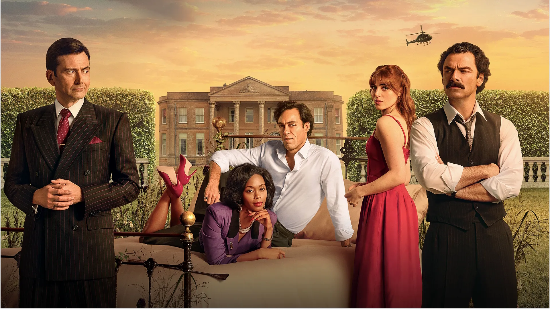 A promotional poster for the TV show "Rivals" featuring several main cast members posing outdoors with a large stately manor house in the background under a warm twilight sky, including David Tennant in a dark pinstripe suit, Aidan Turner with a mustache and crossed arms, and other characters on and around an outdoor bed.