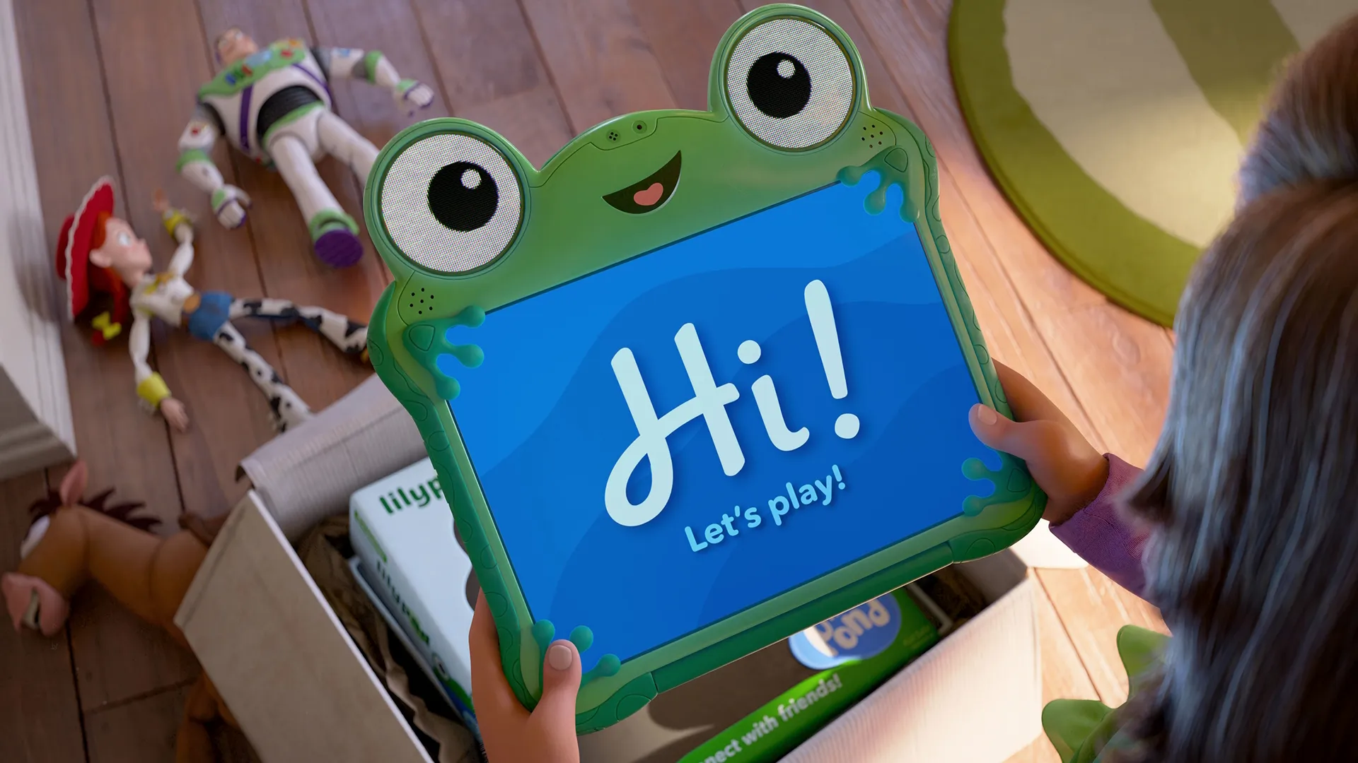 Una imagen promocional oficial de Toy Story 5 de Disney y Pixar muestra las manos de una niña desempaquetando una tableta inteligente verde con forma de rana llamada Lilypad (Greta Lee) con el mensaje "¡Hola! ¡Juguemos!" en la pantalla azul, mientras que los juguetes clásicos Buzz Lightyear (Tim Allen), Jessie (Joan Cusack) y Tiro al Blanco están en el suelo tirados