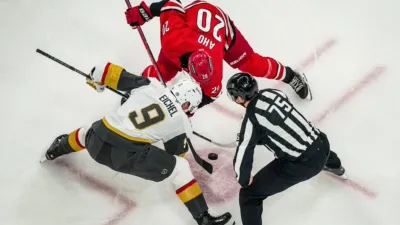A top-down view of the referee, Jack Eichel of the Vegas Golden Knights, and Sebastian Aho of the Carolina Hurricanes during an NHL match.