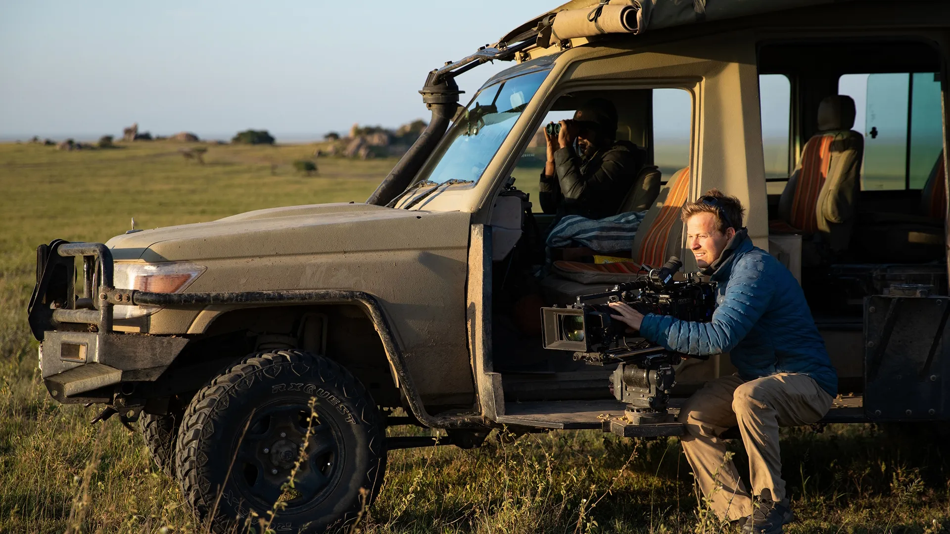 Bertie Gregory sits next to a safari Jeep filming wildlife.  (credit: National Geographic/Jigar Ganatra)