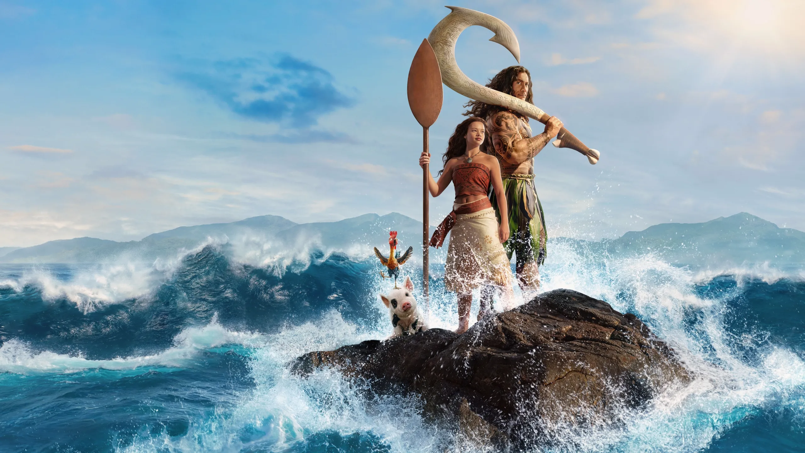 A live-action Moana stands holding a paddle next to Maui on a rocky outcrop surrounded by crashing ocean waves, accompanied by the rooster Heihei and the pig Pua.