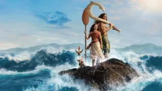 A live-action Moana stands holding a paddle next to Maui on a rocky outcrop surrounded by crashing ocean waves, accompanied by the rooster Heihei and the pig Pua.