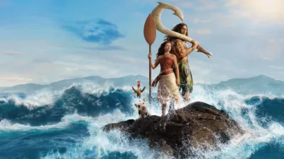 A live-action Moana stands holding a paddle next to Maui on a rocky outcrop surrounded by crashing ocean waves, accompanied by the rooster Heihei and the pig Pua.