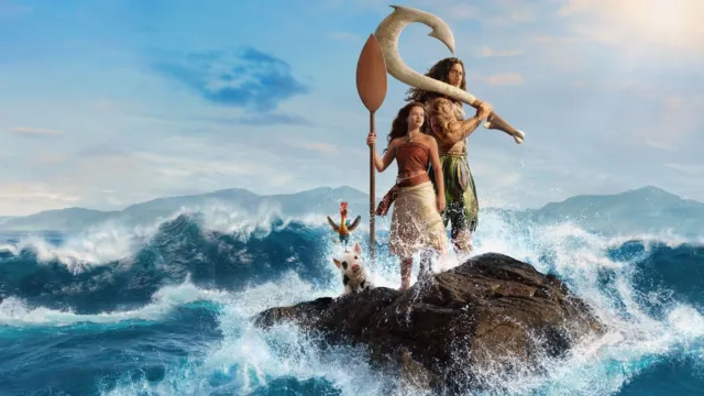 波が打ち寄せる岩場に、実写版のモアナがマウイの隣でパドルを手に立っている。そばには、ニワトリのヘイヘイとブタのプアもいる。