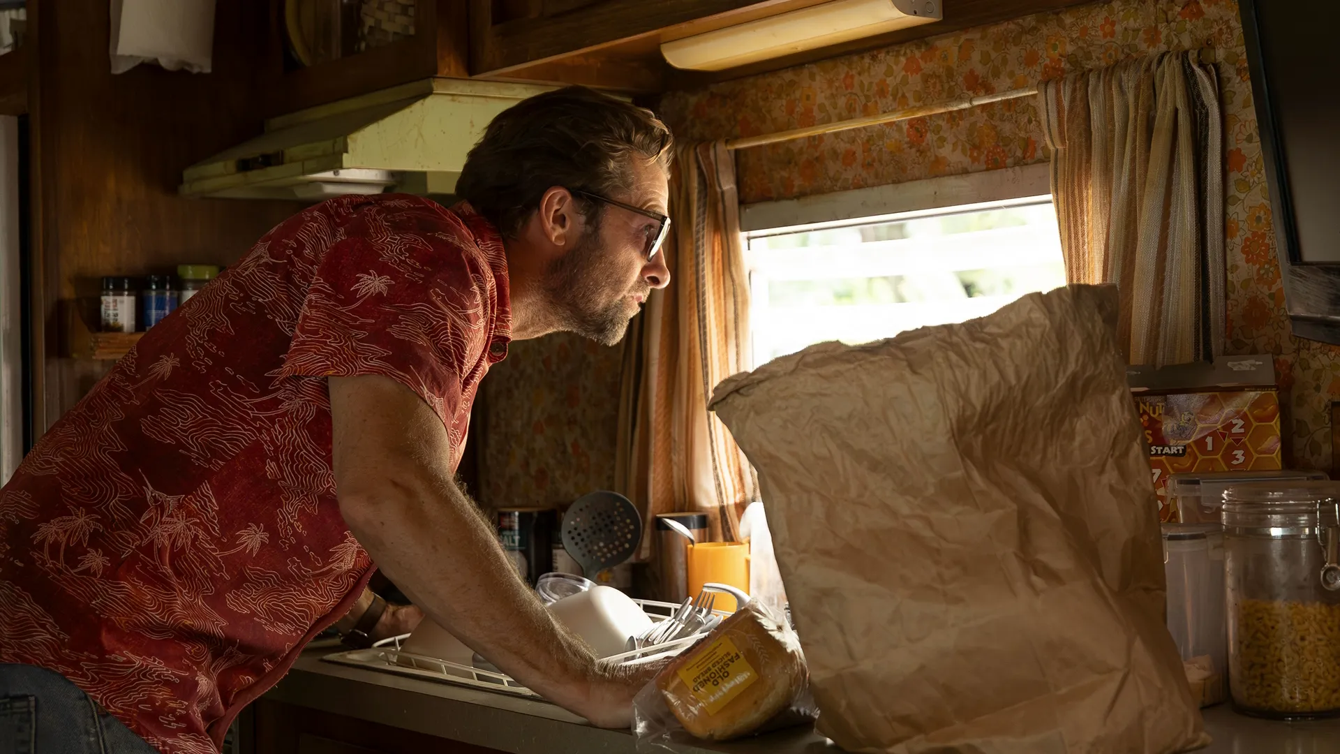 RJ (Scott Speedman) inside a messy trailer kitchen, peering out of a window