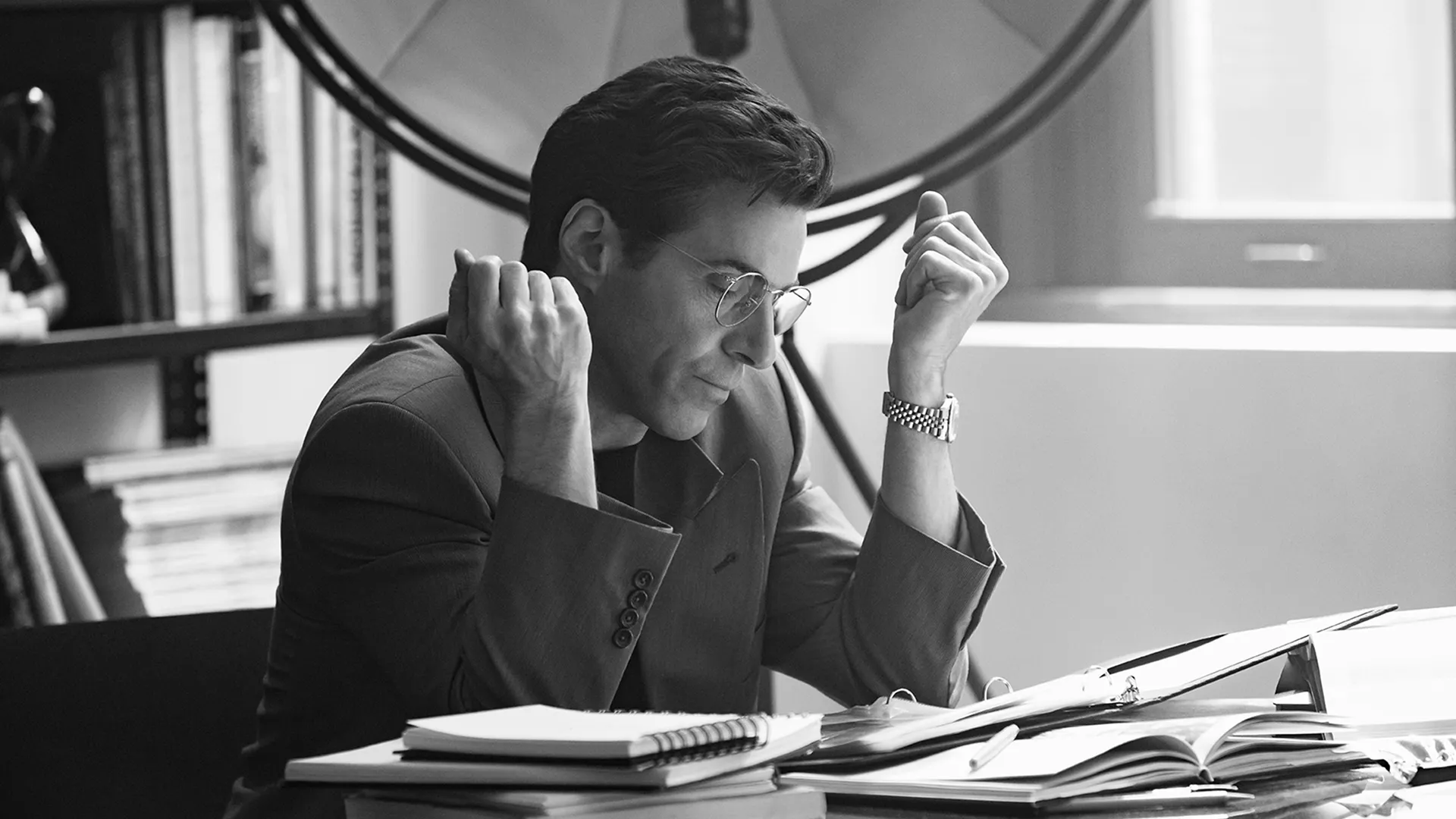 A focused John F. Kennedy Jr. (Paul Kelly) at his desk in a black and white set photo from FX's Love Story.