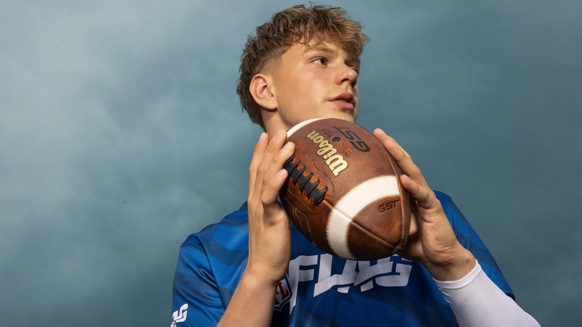 Close-up of a young man holding the football in both hands as he scans the field.